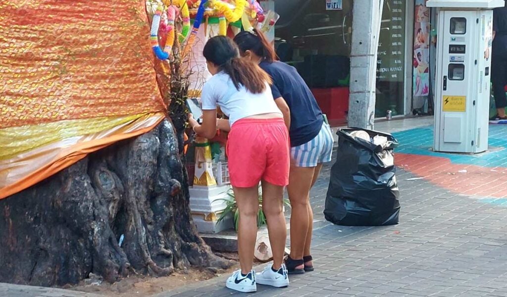 two Thai women searching for lucky numbers in the bark of a tree in Pattaya