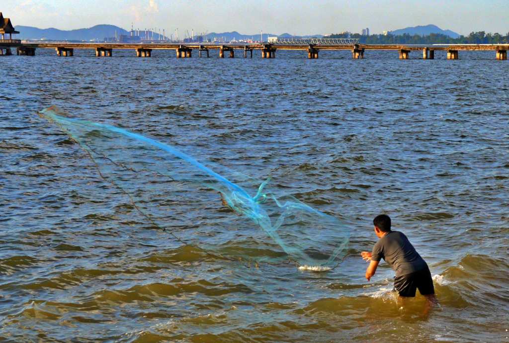 Man fishing with a throwing net at Krating Lai beach in Pattaya