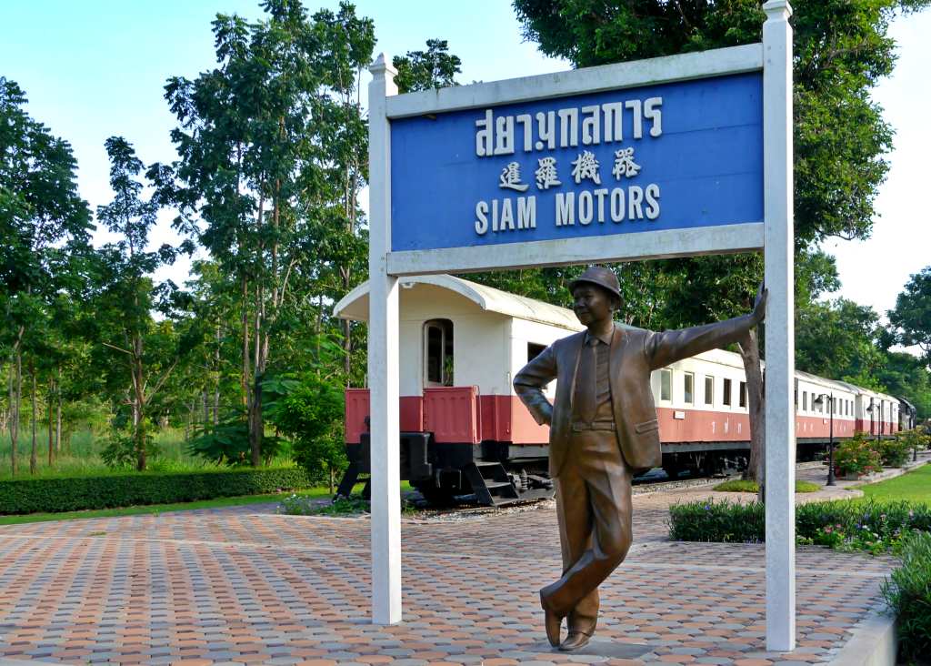 Statue of Mr Pornprapha leaning on the siam motors railway sign